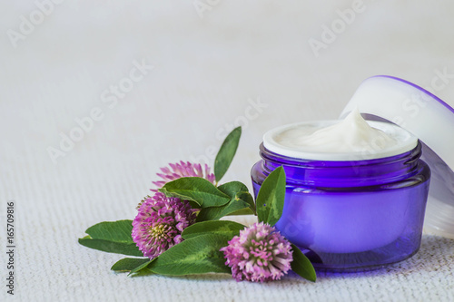  Natural cosmetic. A jar with cream for face and body skin care and fresh clover flowers on a light background.