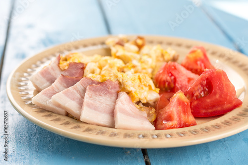 Flat lay fried eggs breakfast with domestic raw bacon and tomato salad