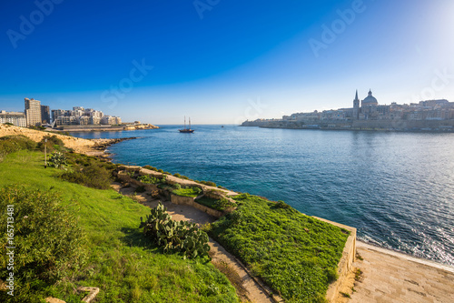 Valletta, Malta - Skyline view of the ancient city of Valletta and Sliema at sunrise shot from Manoel island at spring time with sailing boat, St.Paul's cathedral, blue sky and green grass