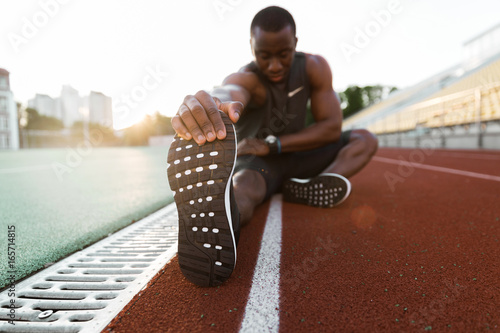 Young concentrated african male athlete stretching legs photo