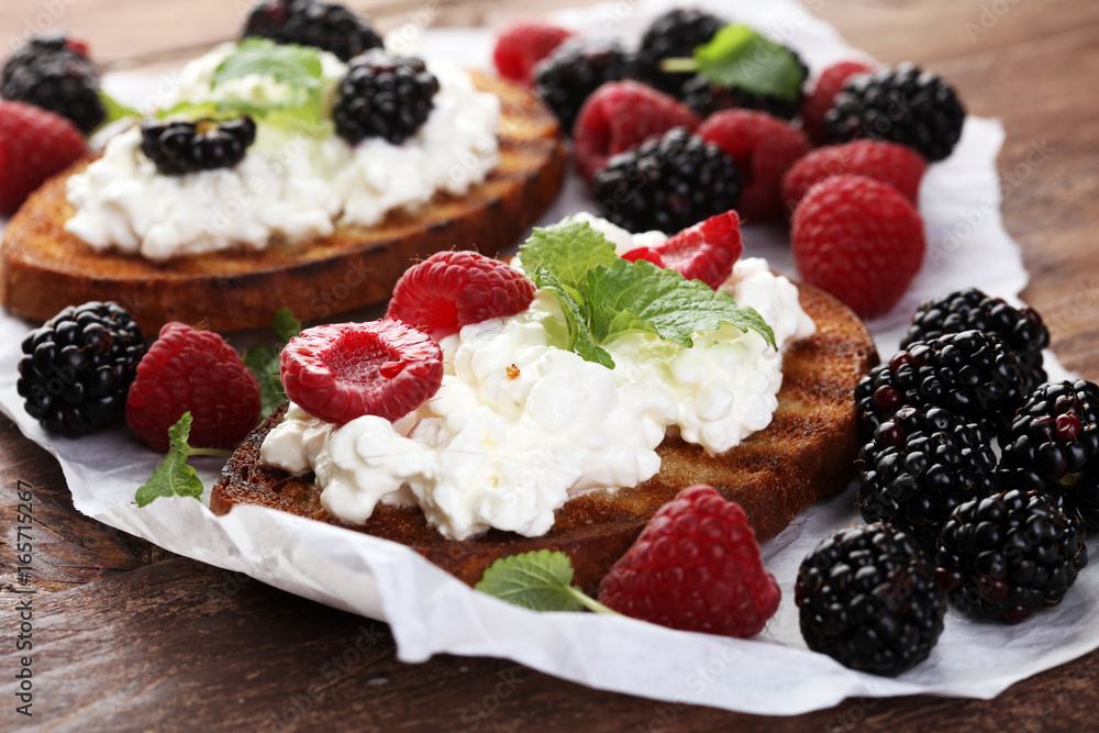 Bread with cheese cream and blackberries and raspberries for lunch table. Sharing antipasti on party or summer picnic time over wooden rustic background.