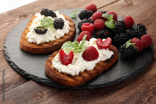 Bread with cheese cream and blackberries and raspberries for lunch table. Sharing antipasti on party or summer picnic time over wooden rustic background.