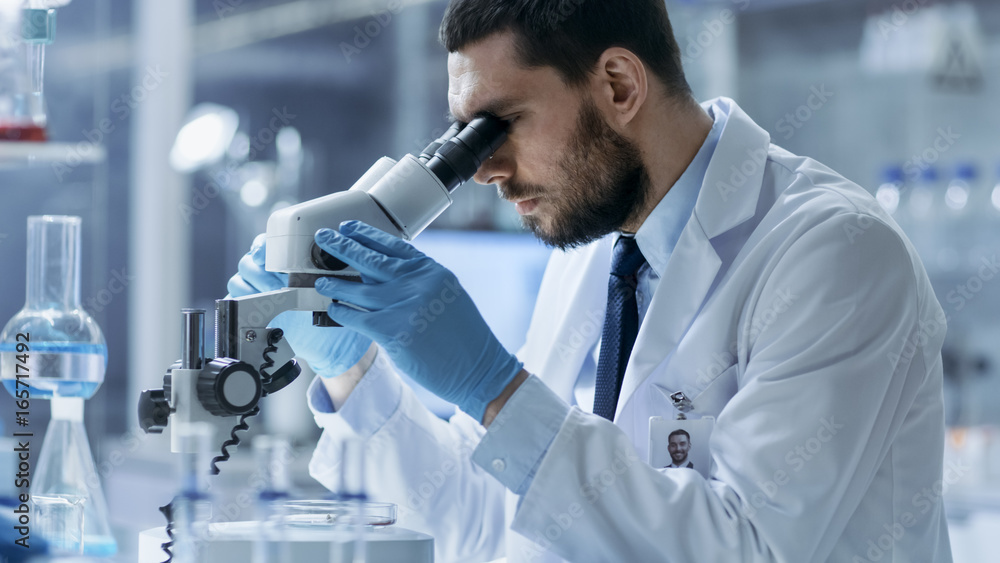 Research Scientist Looks into Microscope. He's Conducts Experiments in Modern Laboratory. Research Scientist Looks into Microscope. He's Conducts Experiments in Modern Laboratory.