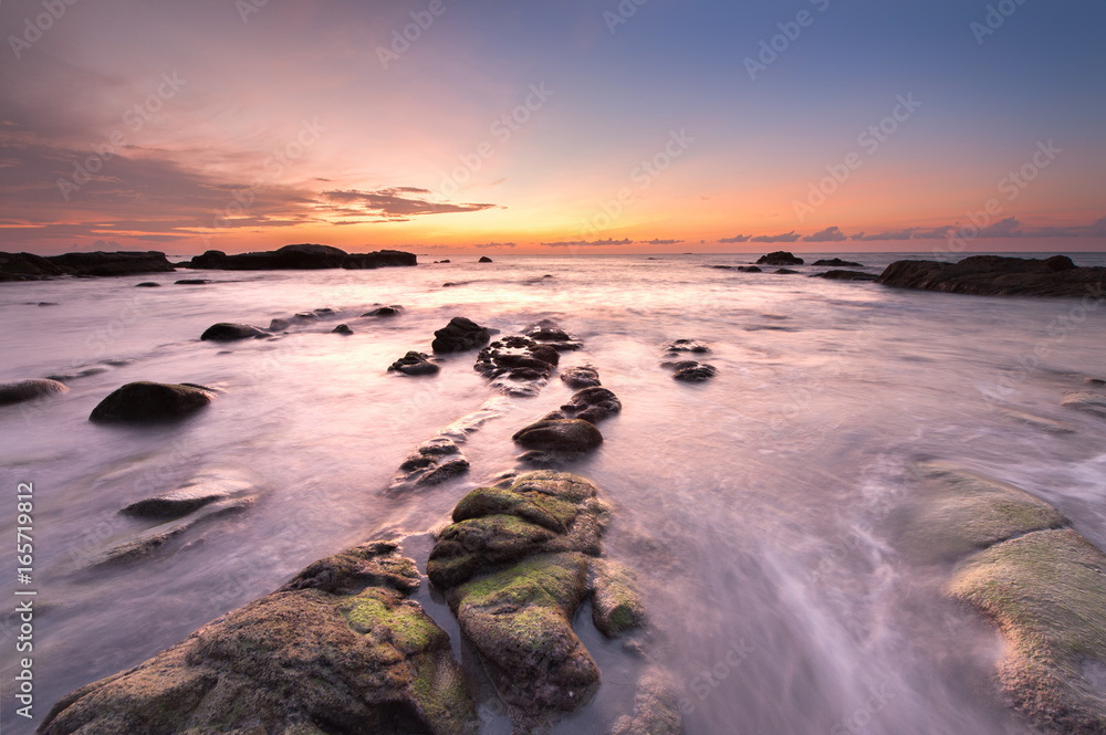 Colorful sunset with natural coastal rocks covered by green moss. Image contain soft focus due to long exposure.