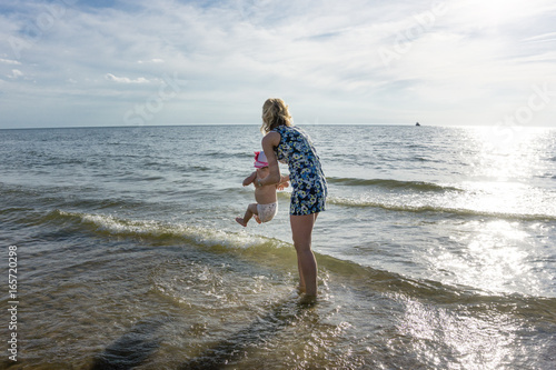 Happy young woman in dress is playing with child girl on the beach