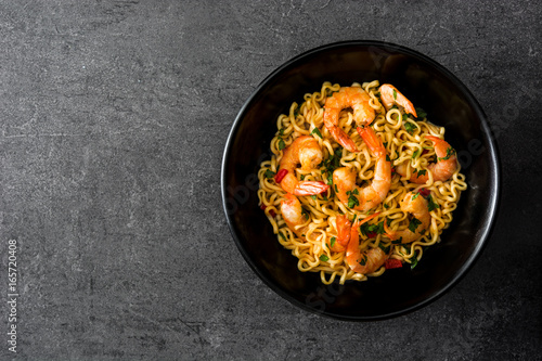 Noodles and shrimps with vegetables in black bowl on black stone

