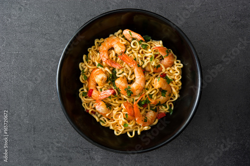 Noodles and shrimps with vegetables in black bowl on black stone