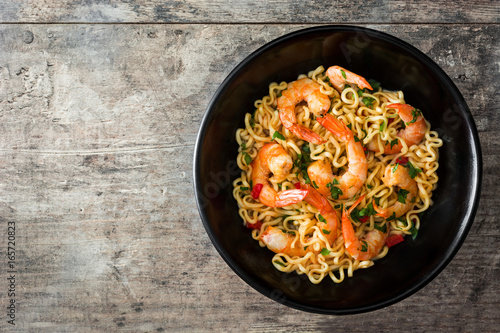 Noodles and shrimps with vegetables in black bowl on wooden table