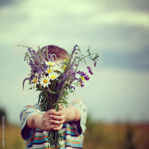 Little kid boy holding bouquet of fields flowers. Child giving flowers.