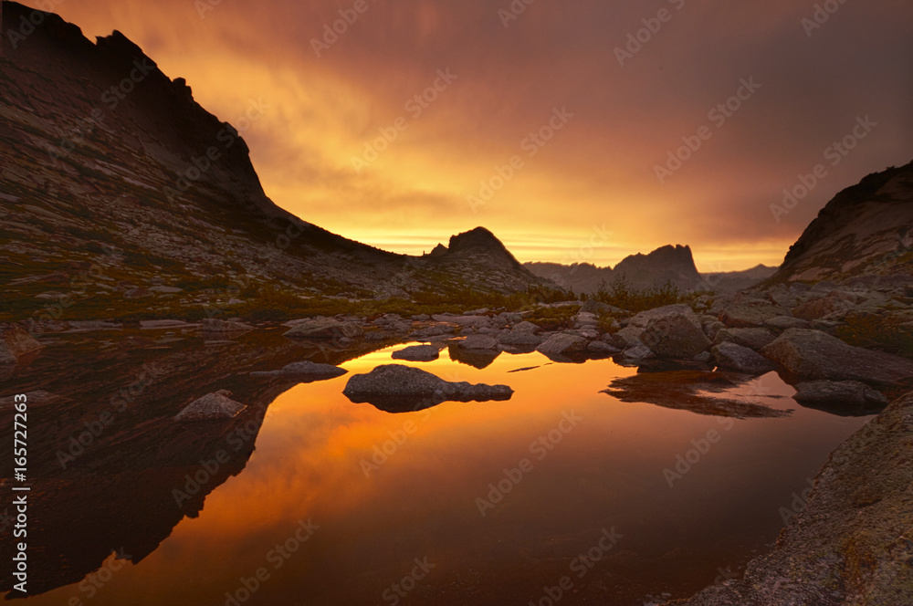 Sunset in mountains near lake. Sunlight reflected on mountain tops. Golden light from sky reflected in a mountain lake. Ergaki