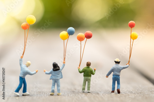 Family and kid concept. Group of children miniature figure with colorful balloons standing, walking and playing together on wooden table. photo