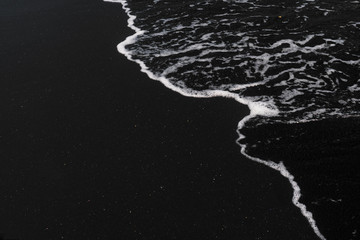 Poster Zwart Wit oceaanschuim op zwart vulkanisch zand  © glass_frog