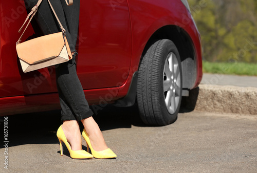 Young woman with slim legs in high heels near car