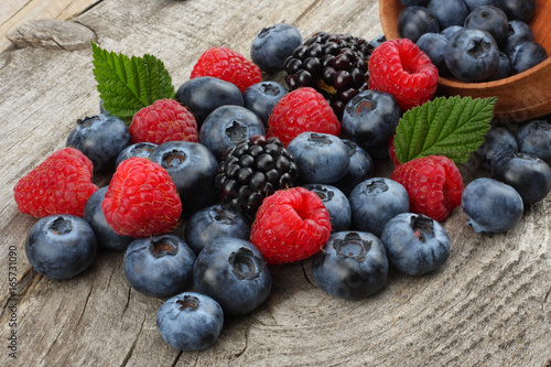 Fotografie mix of blueberries, blackberries, raspberries in wooden bowl on old wooden table