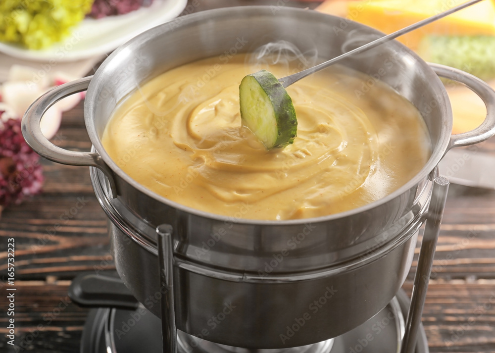 Pot of delicious cheese fondue with dipped cucumber on wooden table Pot of delicious cheese fondue with dipped cucumber on wooden table