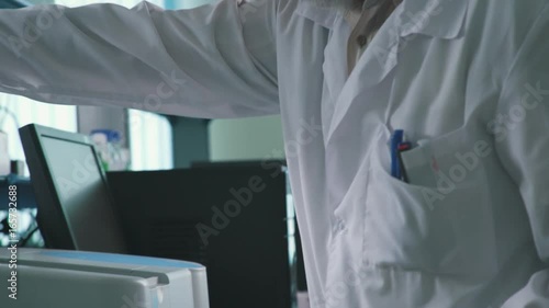 A scientist with glasses and a beard in a white sterile dressing gown works in the laboratory and conducts an experiment. A concentrated and colorful male engineer works with high-tech equipment. photo