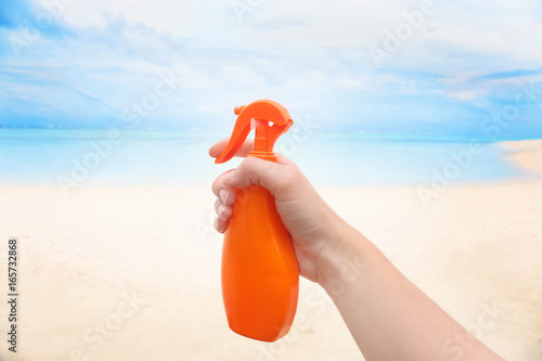 Female hand with bottle of sunscreen cream and blurred sea beach on background. Summer vacation concept