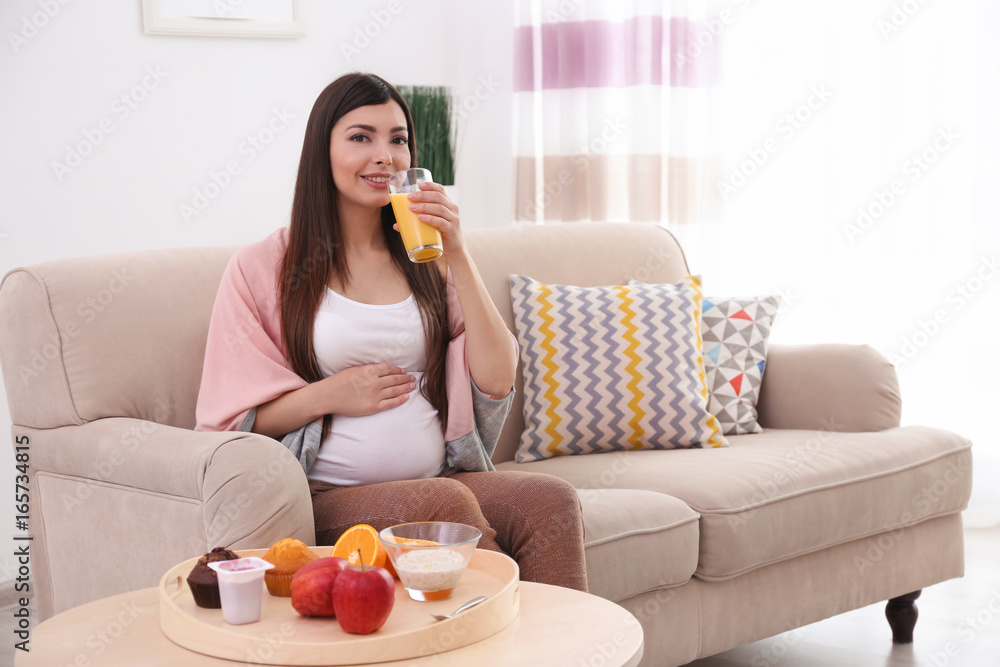 Pregnant woman sitting near table with breakfast and drinking juice