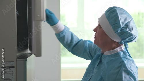 Woman lab assistant in blue sterile clothes - hat and gloves - works in a chemical laboratory with reagents. Researcher conducts experiments and fixes the reballutates. Work in scientific laboratory photo