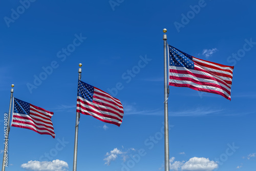 Three US flags and bright blue sky.