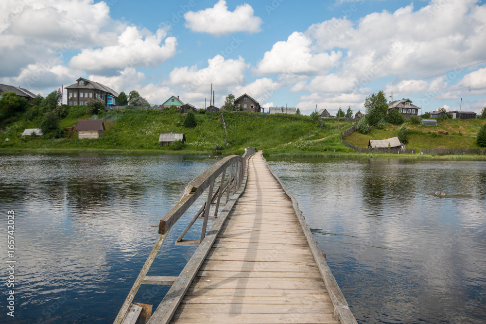 north Russian village Isady. Summer day, Emca river, old cottages on the shore, old wooden bridge and clouds reflections. north Russian village Isady. Summer day, Emca river, old cottages on the shore, old wooden bridge and clouds reflections.