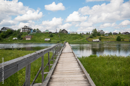 north Russian village Isady. Summer day  Emca river  old cottages on the shore  old wooden bridge and clouds reflections.