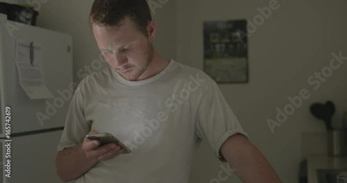 Man checks his smartphone in the morning in his kitchen.