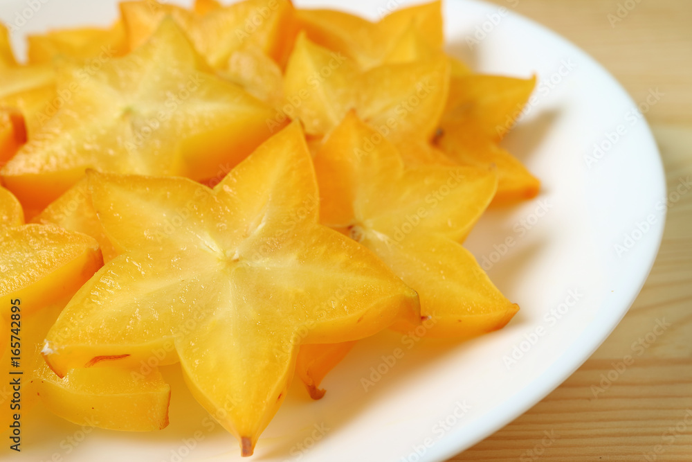 Closed up vibrant color fresh Star Fruit sliced in many pieces served on white plate 