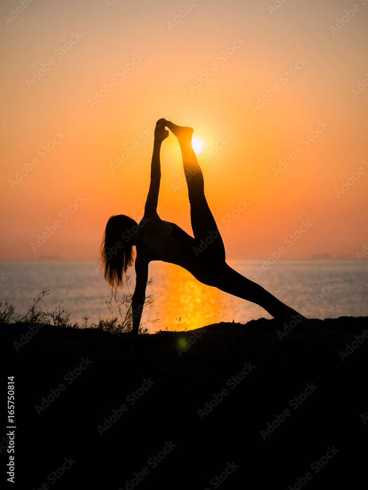Silhouette young woman practicing yoga on the beach above sea at amazing sunset. fitness, sport, yoga and healthy lifestyle concept.
