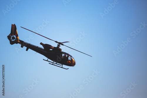 A flying black helicopter aircraft during the flight with blue sky in the background