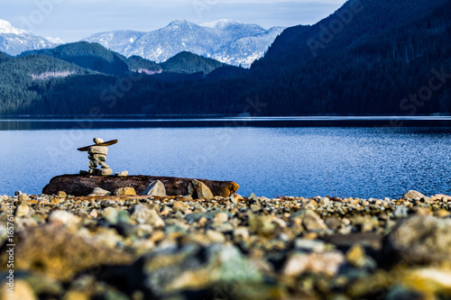inukshuk on rocky shore with mountains and lake photo