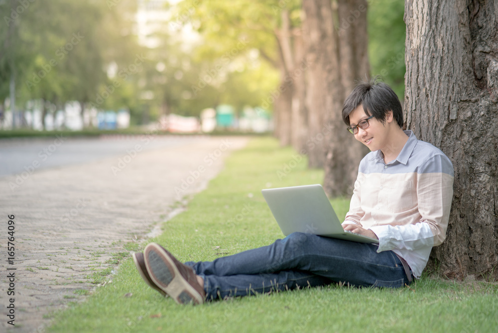 Young Asian happy man using laptop computer in the garden, male university student relaxing outdoor, education and technology concepts Young Asian happy man using laptop computer in the garden, male university student relaxing outdoor, education and technology concepts