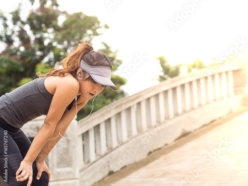 Female runner athlete resting and catching the breath after marathon training in the park at sunset, Standing bent over 