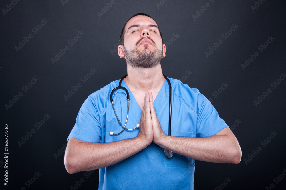 Doctor wearing scrubs with stethoscope praying Doctor wearing scrubs with stethoscope praying