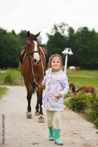 Little girl is leading a horse to a riding training outdoors