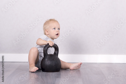 Sport is life. Funnybaby boy sitting on the floor with kettlebell. Copy space