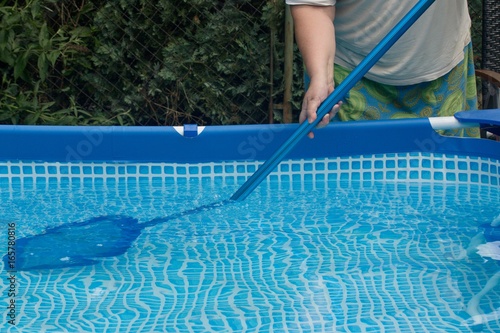 Person cleaning garden pool from leaves, insects and debris using a skim net on pole