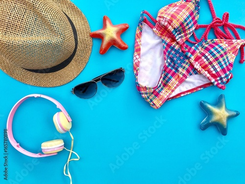 The concept of accessories for summer.CloseupA brown woven hat,sunglasses,pink headphone and colorful swimsuit with blue & orange starfish set on blue background.Copy space with Selective focus.