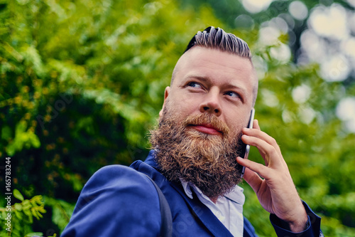 Portrait of bearded hipster male using smartphone outdoor.