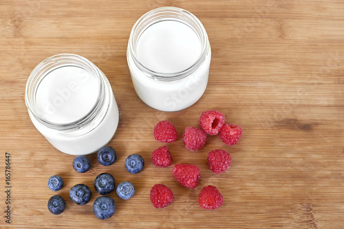 Yogurt in glass jar, raspberries and blueberries on a wooden background - directly above