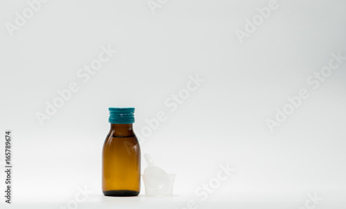 Fototapeta Naklejka Na Ścianę i Meble -  Cough syrup in amber bottle with blank label and a plastic measuring cup, teaspoon on white background