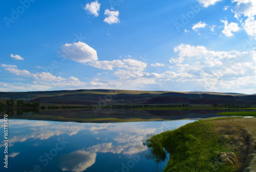 View of calm lake, hills, green grass and blue sky in Altai mountains. White clouds reflected in water. Chuya steppe, Altay Republic, Siberia, Russia. © Vector DSGNR