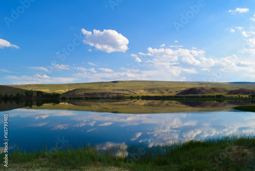 Landscape of calm lake, hills, green grass and blue sky in Altai mountains. White clouds reflected in water. Chuya steppe, Altay Republic, Siberia, Russia. © Vector DSGNR