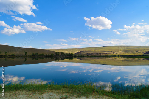 Fototapeta Naklejka Na Ścianę i Meble -  View of quiet lake, hills, green grass and blue sky in Altai mountains. White clouds reflected in water. Chuya prairie, Altay Republic, Siberia, Russia.