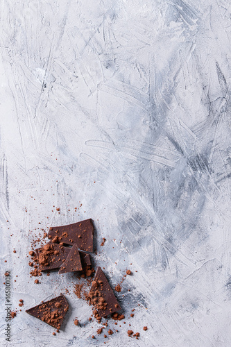 Chopped dark chocolate with cocoa powder over gray concrete texture background. Top view with copy space.