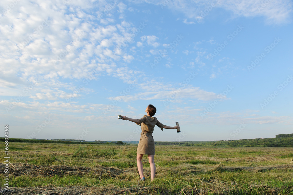 A young girl with alternative coffee brewing stands with her back against the background of summer field A young girl with alternative coffee brewing stands with her back against the background of summer field