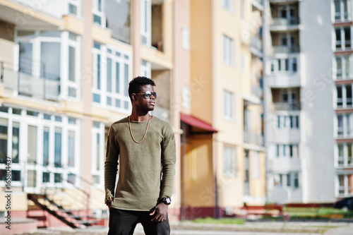 Handsome and attractive african american man in sunglasses posing next to the tall building on a street.