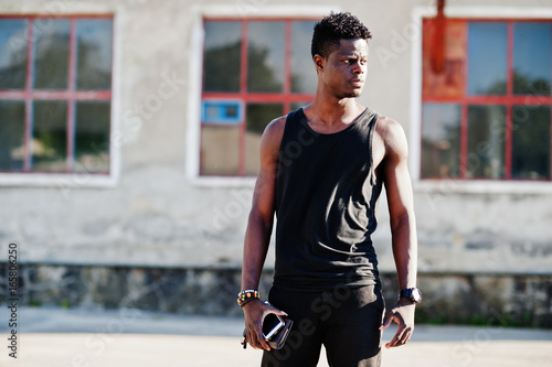 Portrait of a handsome african american guy in black muscle shirt posing in industrial zone.