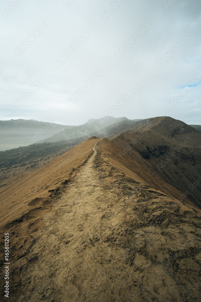 a path on a Bromo volcano rim in Indonesia. Volcano ashes are full on the path after the eruption. The road look long forward to nowhere. 