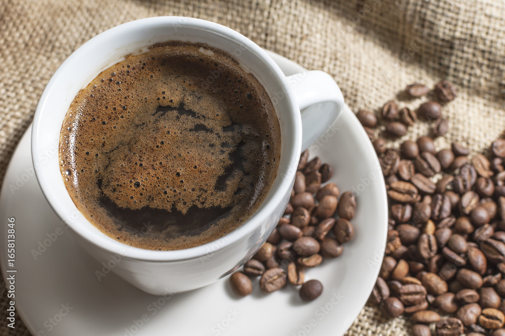 Fototapeta premium Hot cup of coffee with coffee beans on canvas.